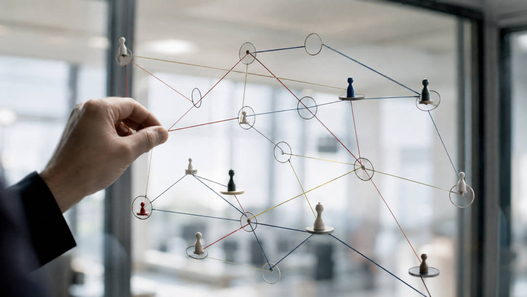 Hand attaching a connection between game pieces on a glass wall, symbolic image for game theory